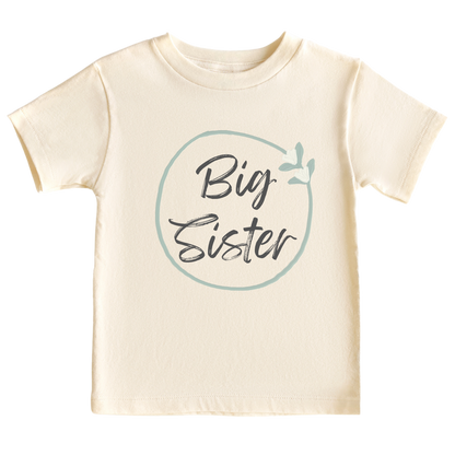 Natural kid's t-shirt with a minimalistic printed graphic of a pastel green floral wreath and the text 'Big Sister.' This delightful t-shirt celebrates the exciting role of a big sister.