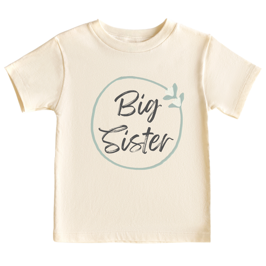 Natural kid's t-shirt with a minimalistic printed graphic of a pastel green floral wreath and the text 'Big Sister.' This delightful t-shirt celebrates the exciting role of a big sister.