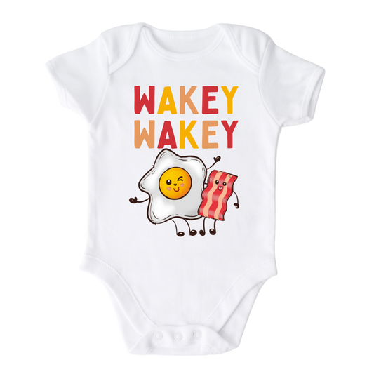 White Baby Onesie with a charming graphic of an egg and bacon, accompanied by the text 'Wakey Wakey.' Ideal for children who love breakfast and waking up with a smile. 