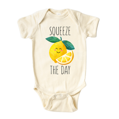 Natural Baby Bodysuit showcasing a playful printed graphic of a lemon with the text 'Squeeze The Day.' Explore this vibrant and motivational tee, perfect for adding a burst of positivity to your child's wardrobe.