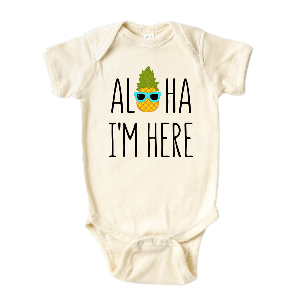 A kids' t-shirt with a pineapple wearing glasses and the text 'Aloha I'm Here.' This fun and tropical design captures the playful spirit, adding a vibrant touch to the wearer's style.