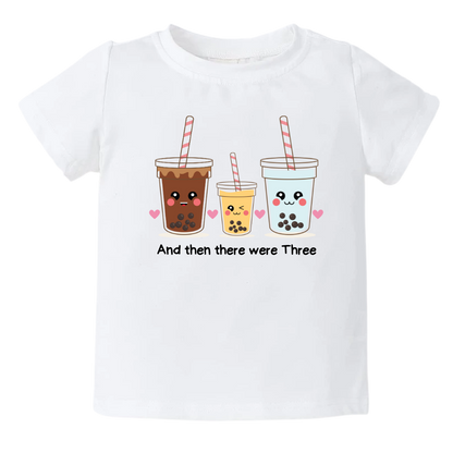 White Tshirt featuring an endearing printed graphic of a Milk Tea family and the heartwarming text 'And Then There Were Three.' Celebrate the joy of family with this delightful tee, perfect for little ones and proud parents.